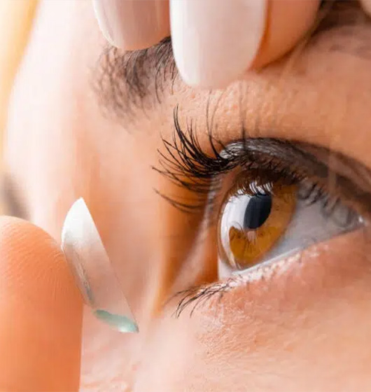 A female inserting a contact lens into her left eye.